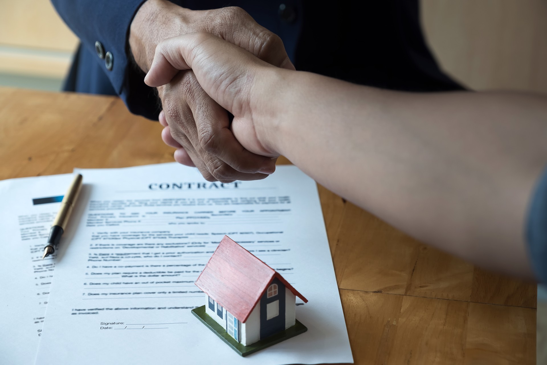 Estate agent shaking hands with his customer after contract signature, Contract document and house model on wooden desk