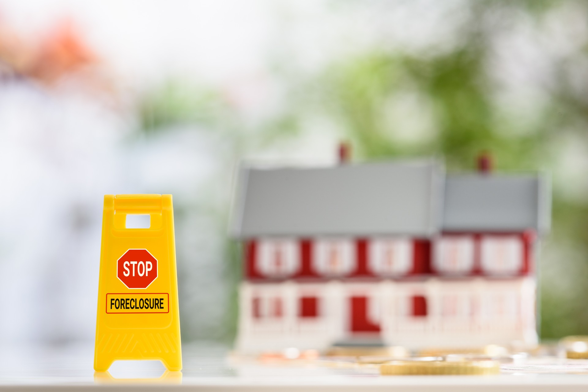 Strategies or ways to stop foreclosure or avoid foreclosure, mortgage relief, financial concept : Yellow sign board with the words STOP FORECLOSURE, a red-white two story house with coins on a table.